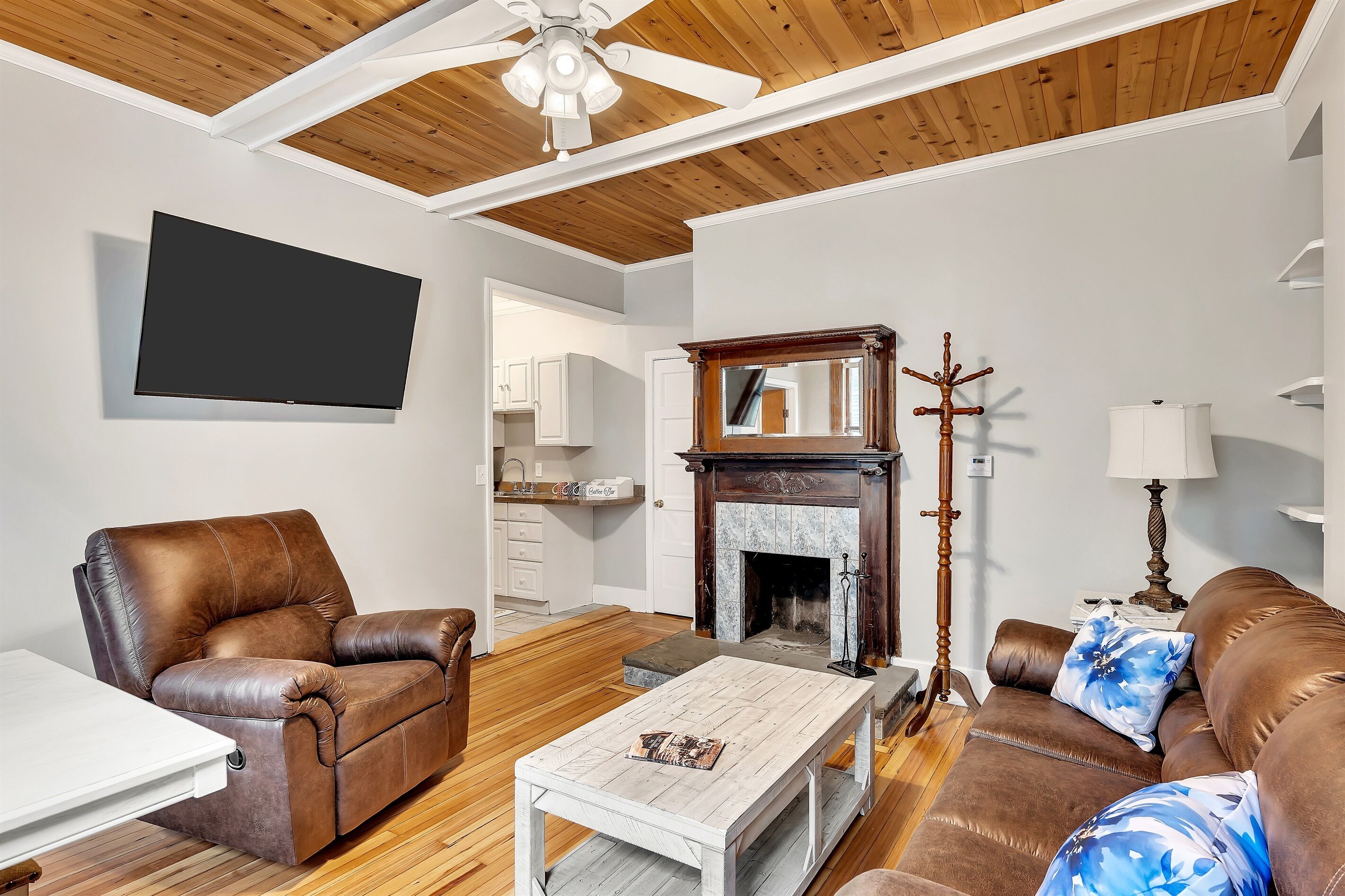 A living room with a brown leather sofa, a white coffee table, a fireplace, and a television mounted on the wall.