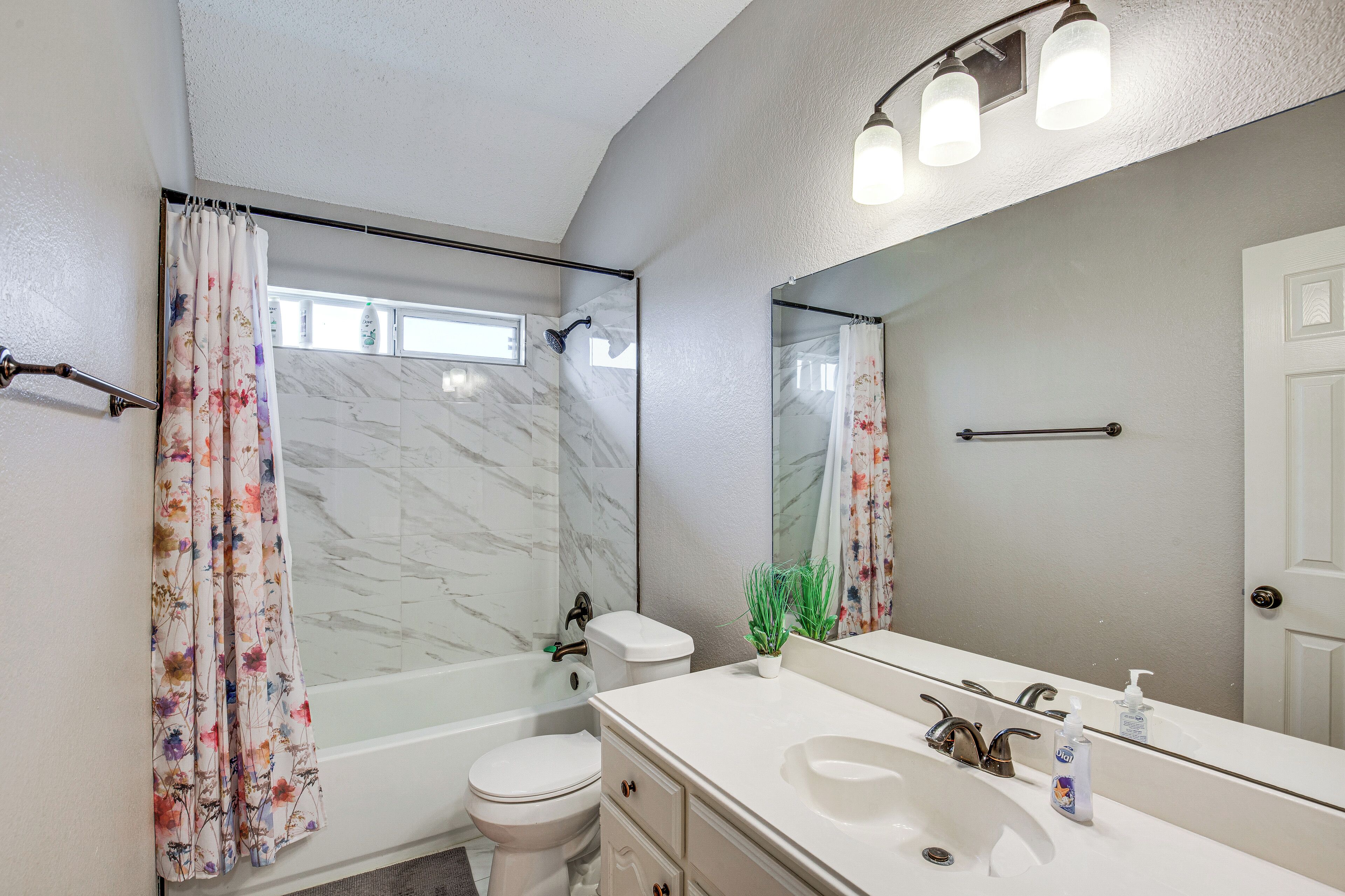 A bathroom with a shower, toilet, sink, and a large mirror.