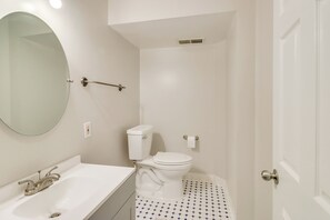 Ein Badezimmer mit einem weißen Waschbecken, einem runden Spiegel, einer Toilette und einer Tür.