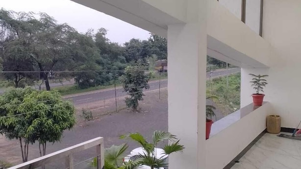 A modern hotel balcony with potted plants, a glass railing, and a view of the road and greenery. - Hotel Moonlight & Restaurant (Sehore)