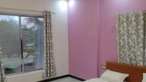 A bedroom with a bed, a ceiling fan, a window with curtains, and a pink wall. - Hotel Moonlight & Restaurant (Sehore)