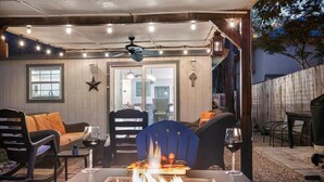 Een terras buiten met een vuurplaats, zitplaatsen en uitzicht op het huis.