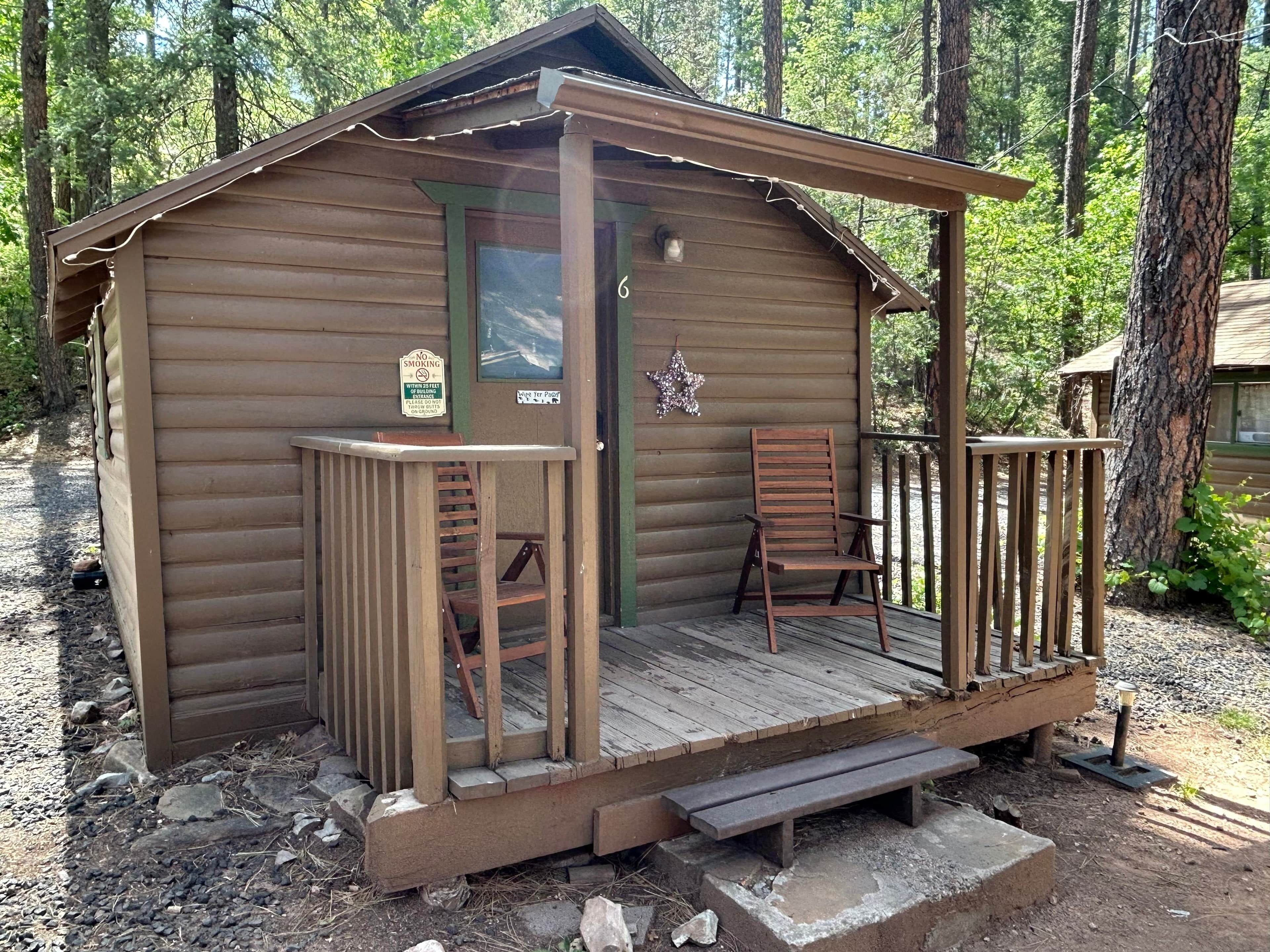 A small wooden cabin with a porch, a chair, a bench, and a 'No Smoking' sign.