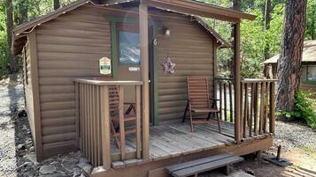 A small wooden cabin with a porch, a chair, a bench, and a 'No Smoking' sign.