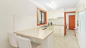 Une cuisine de taille réduite avec des meubles blancs, un évier, un plan de travail et un réfrigérateur.