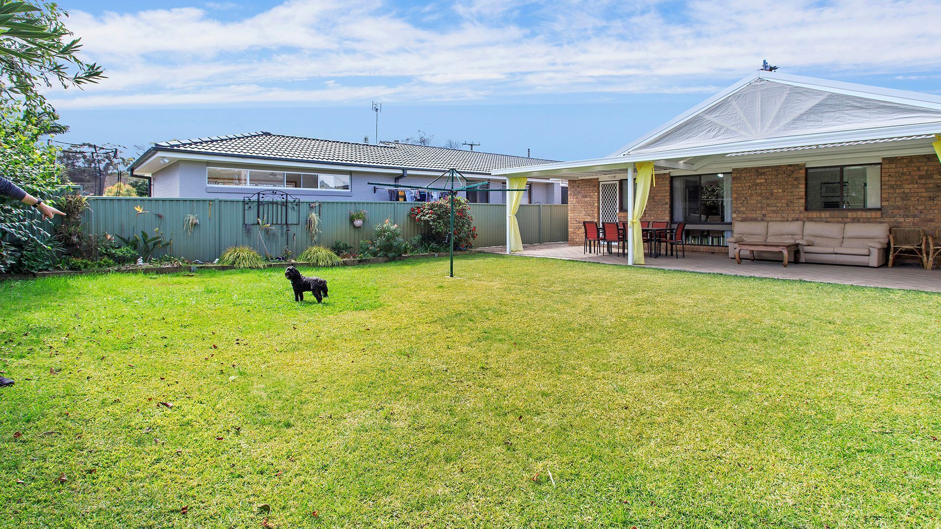 Un jardin avec un chien, une terrasse couverte et une maison avec un toit en tuiles.