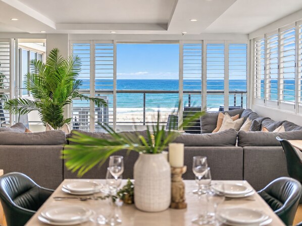 A dining area with a view of the ocean, a sofa, and a table set for dining. - Absolute Beachfront 3BR Apartment | Pool, Spa, Tennis & Ocean Views (Surfers Paradise)