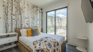 A bedroom with a large bed, a nightstand, a dresser, and a window with a view of buildings. - Fun in Canyons Village-Pet friendly at Canyons Resort + Pool, Gym, and Game Room (Park City)