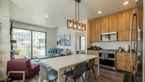 A modern kitchen with wooden cabinets, a stainless steel refrigerator, and a dining area with a white table and chairs. - Fun in Canyons Village-Pet friendly at Canyons Resort + Pool, Gym, and Game Room (Park City)