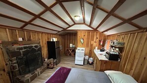 Een knus vakantiehuisje met een stenen open haard, houten wanden, een bed, een kitchenette en een eethoek.