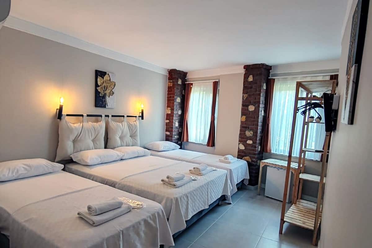 A hotel room with three beds, a small kitchenette, and a window with curtains.