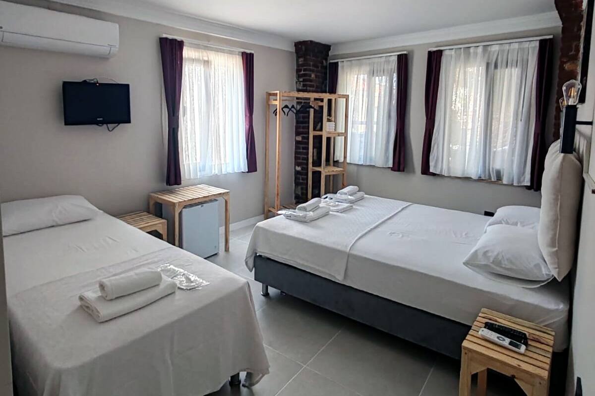 A hotel room with two single beds, a small table, a chair, a TV mounted on the wall, and a brick fireplace.