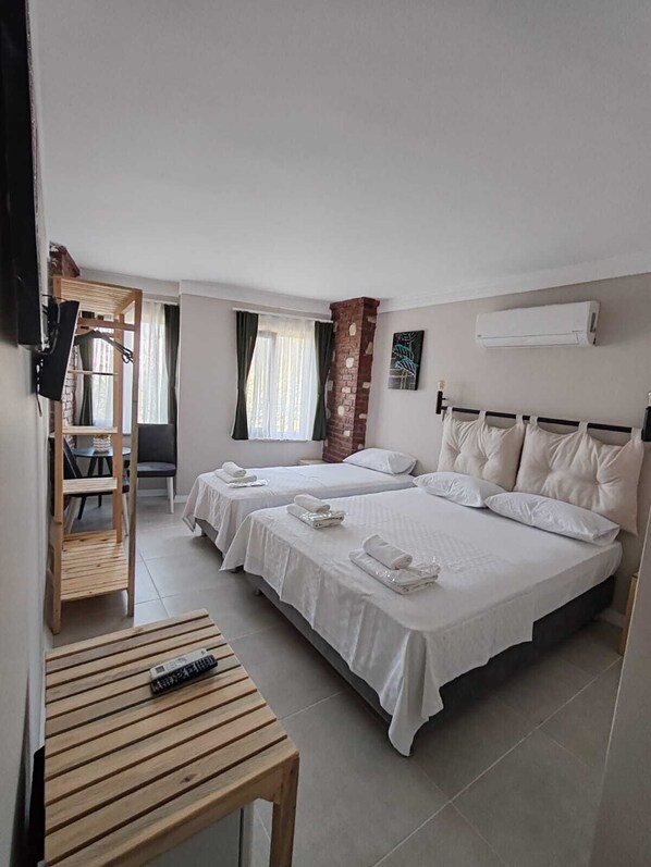 A hotel room with two beds, a wooden table, a TV, and an air conditioning unit. - Aim Bozcaada (Bozcaada)