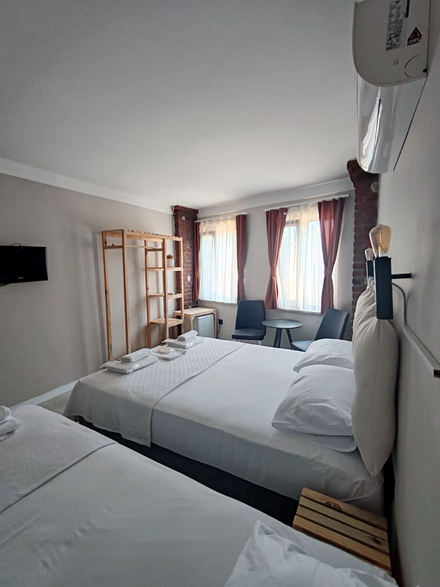 Habitación de hotel con dos camas, un escritorio, una silla, un televisor y una ventana con cortinas.