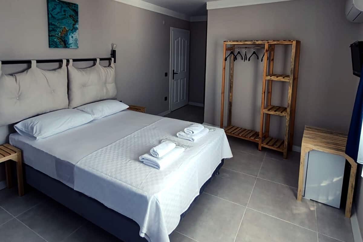 A neatly made bed with white linens and towels, a wooden shelf unit, and a painting on the wall.