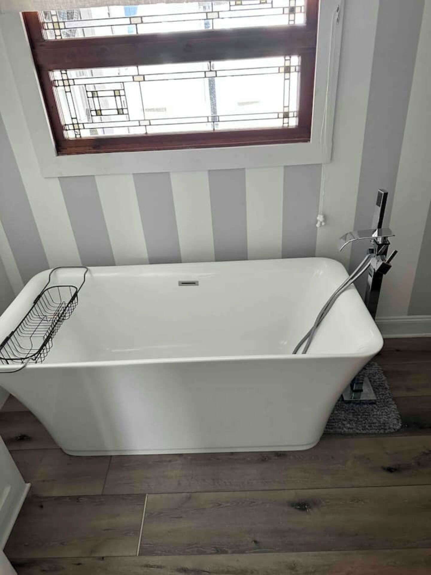 Un baño moderno con una bañera independiente, una ventana sobre ella y suelo de madera.
