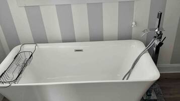 Un baño moderno con una bañera independiente, una ventana sobre ella y suelo de madera.