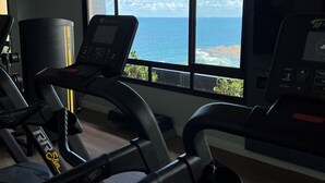 Un gimnasio con cintas de correr, un saco de boxeo y vistas al océano a través de amplias ventanas.