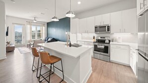 Une cuisine moderne avec des meubles blancs, des appareils en acier inoxydable et un îlot central doté de tabourets de bar.