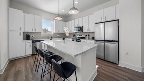 A modern kitchen with white cabinetry, a central island with bar stools, stainless steel appliances, and pendant lighting. - Bright, Spacious 2BD in heart of Tampa | Free Prkg (Tampa)