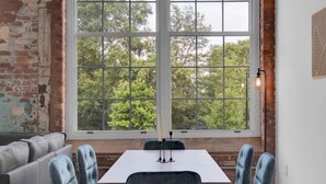 A dining area with a large window, a table, and two blue chairs. - Warm, Cozy 2BD | Pool | Gym | Central! (Greenville)