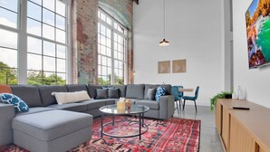 A modern living room with a grey sectional sofa, a round coffee table, and a red patterned rug. - Warm, Cozy 2BD | Pool | Gym | Central! (Greenville)
