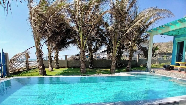 Una piscina cristallina circondata da palme e da una zona ombreggiata.