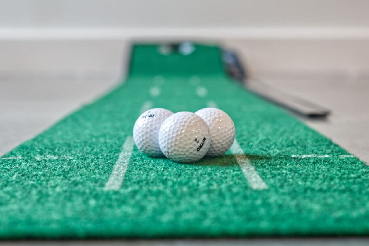 Kolme golfpalloa vihreällä huopamatolla, jossa on valkoisia viivoja – todennäköisesti kyseessä on harjoitusmatto lyhyitä lyöntejä varten.