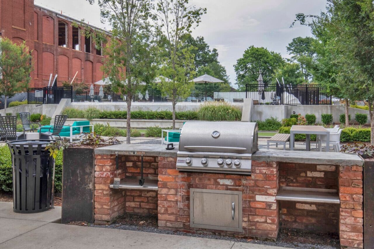 Un espace barbecue extérieur avec un gril en briques, des sièges et une poubelle.