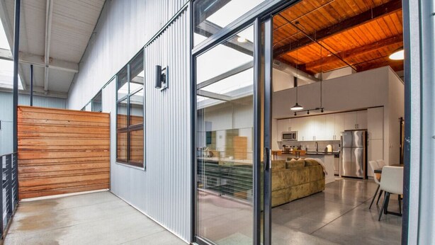 Cozinha moderna com eletrodomésticos de aço inoxidável, um banco de madeira e uma porta de vidro que dá para uma sala de jantar.