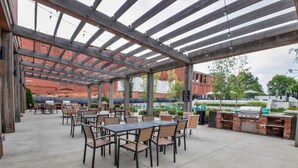 An outdoor patio with tables and chairs, a grill, and a covered area with a view of a brick building. - Huge, Open Loft | Arts District | 5 mins to DT GVL (Greenville)