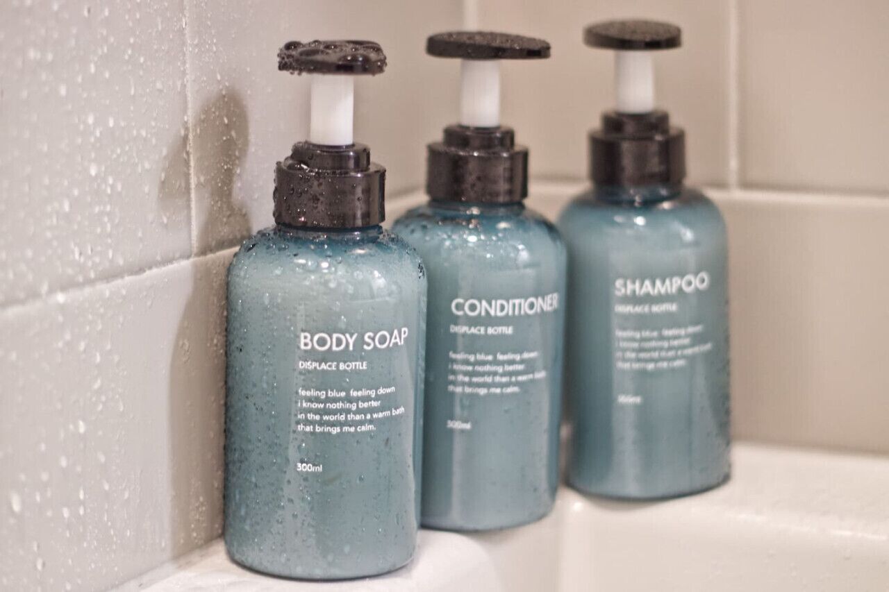 Three bottles of body soap, conditioner, and shampoo on a tiled surface.