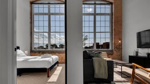 A room with a large window, a bed, a sofa, and a TV. - Bright, Cozy Loft | Pool | Gym | Great location! (Greenville)