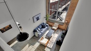A high-ceilinged living room with a large window, a sofa, a coffee table, and a chair. - Bright, Cozy Loft | Pool | Gym | Great location! (Greenville)