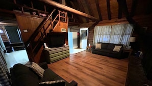 A cozy, rustic living room with wooden floors, a staircase, a sofa, and a television. - Cabin #8 - Ranch House (Payson)