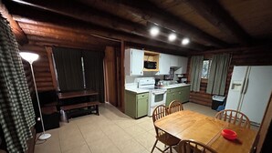 A cozy cabin-style kitchen with a wooden dining table and chairs, a built-in stove, and a refrigerator. - Cabin #8 - Ranch House (Payson)