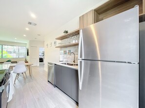 A modern kitchen with a stainless steel refrigerator, wooden cabinets, and a dining area with a table and chairs.
