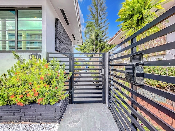 A modern building with a gated entrance, a brick planter with greenery, and a clear blue sky.