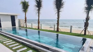 Una piscina infinita moderna con agua cristalina azul, rodeada de palmeras y vista al océano.