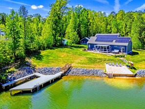 Una propiedad frente al lago con muelle, una casa con paneles solares y una zona de estar exterior cubierta.