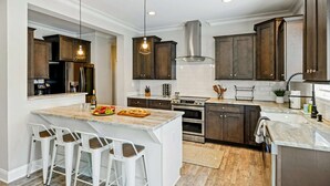 A modern kitchen with a central island, bar stools, dark wood cabinets, stainless steel appliances, and pendant lighting. - Lakefront Lake Anna, Hot Tub, Pool, Beach (Mineral)