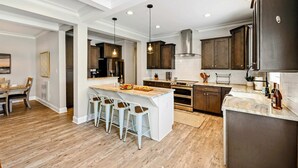 A modern kitchen with a central island, bar stools, wooden cabinets, and stainless steel appliances. - Lakefront Lake Anna, Hot Tub, Pool, Beach (Mineral)