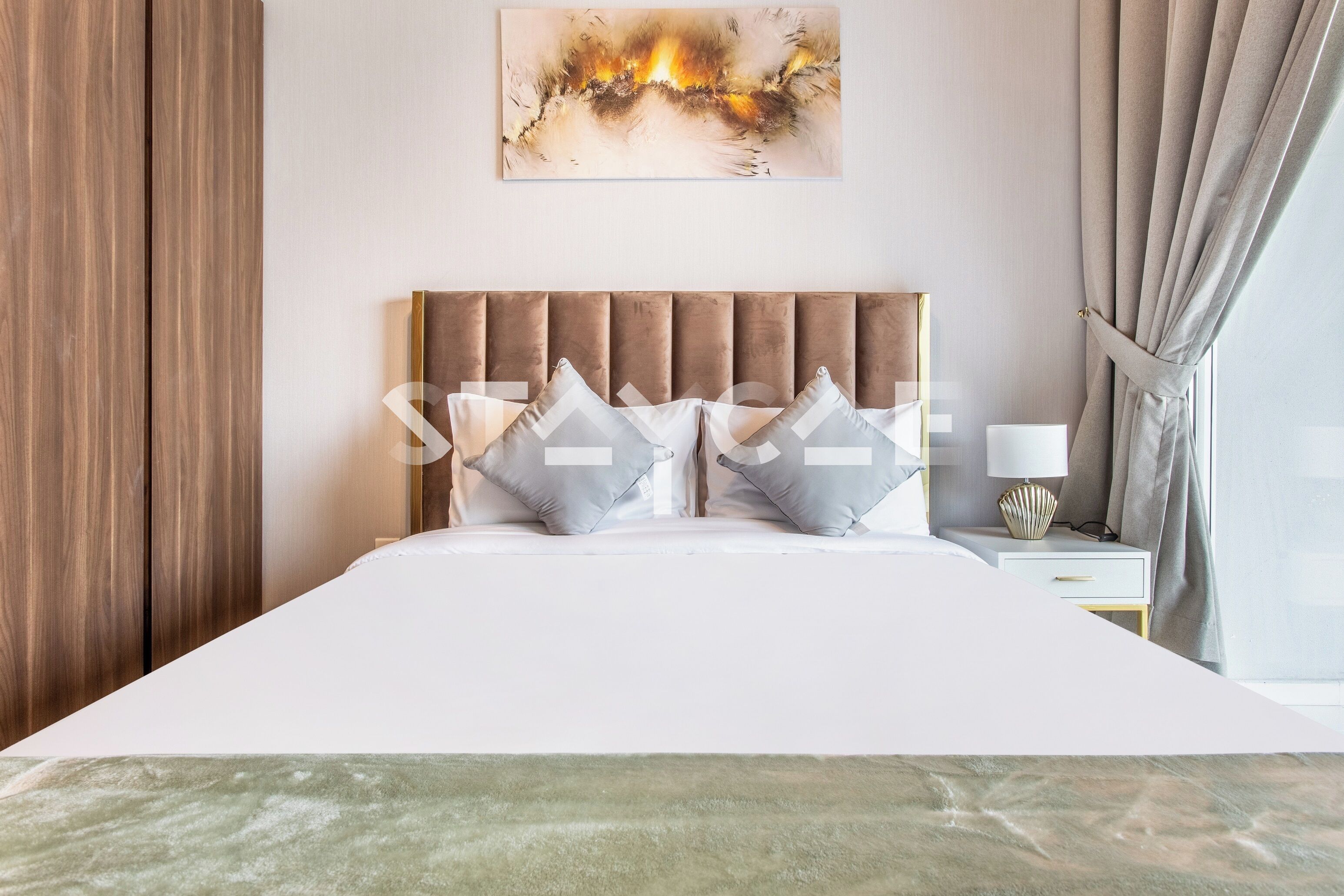 Een moderne hotelkamer met een groot bed, een hoofdbord, een nachtkastje met een lamp en een raam met gordijnen.