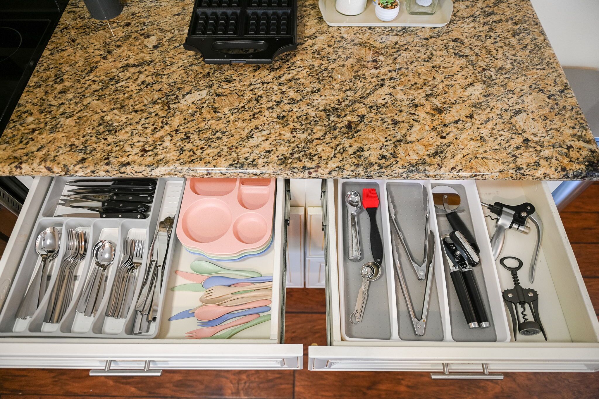 A kitchen counter with a granite top and a drawer below containing various utensils and kitchen tools.