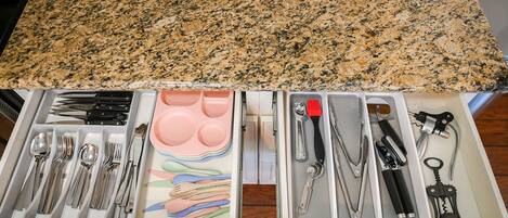 A kitchen counter with a granite top and a drawer below containing various utensils and kitchen tools.