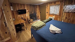 A wooden room with a bed, a TV, a fireplace, and a window with patterned curtains. - Cabin #9 - Studio with fireplace (Gila County)