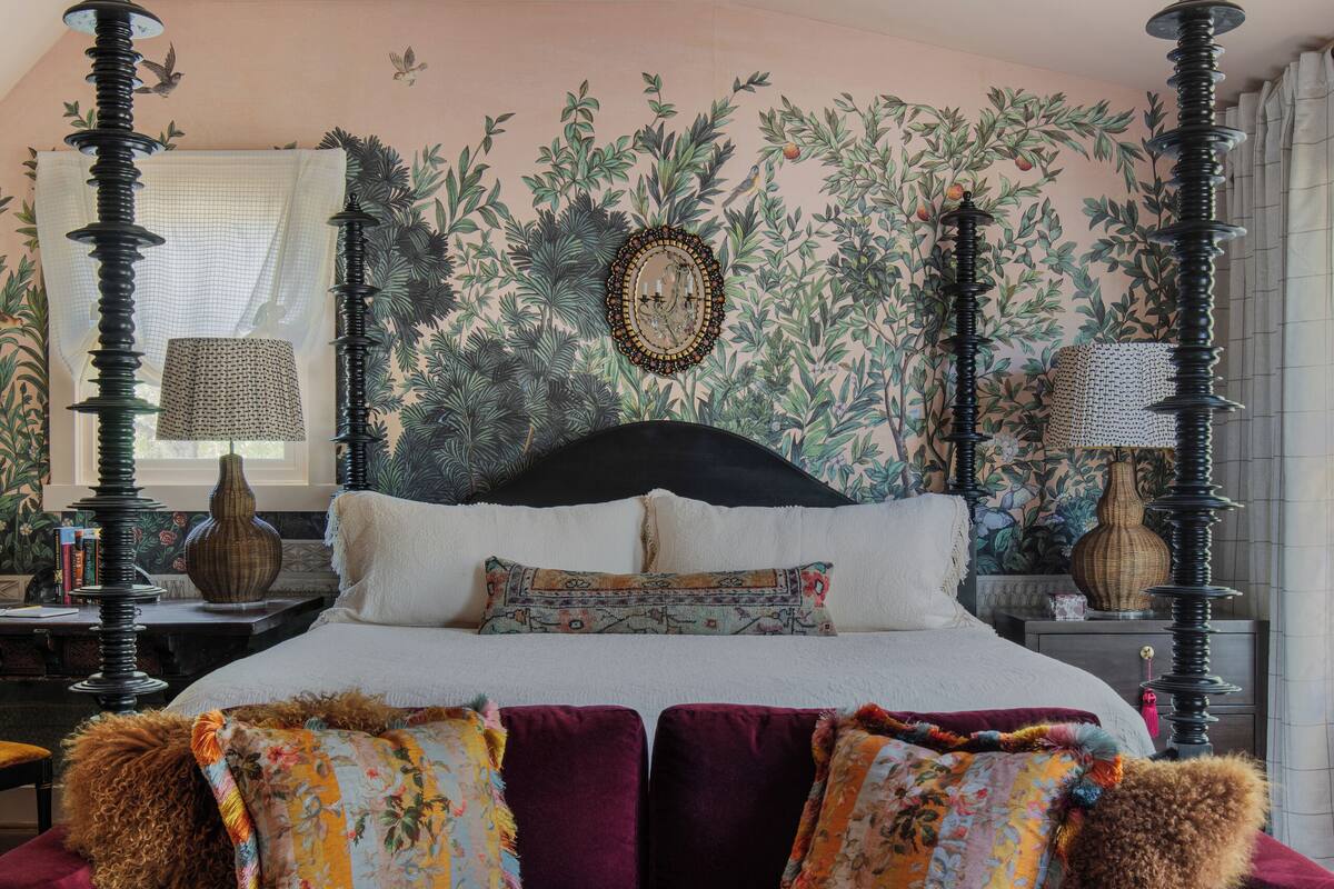 Une chambre à coucher comprenant un lit, un canapé, un lustre et un mur orné d’un motif végétal.
