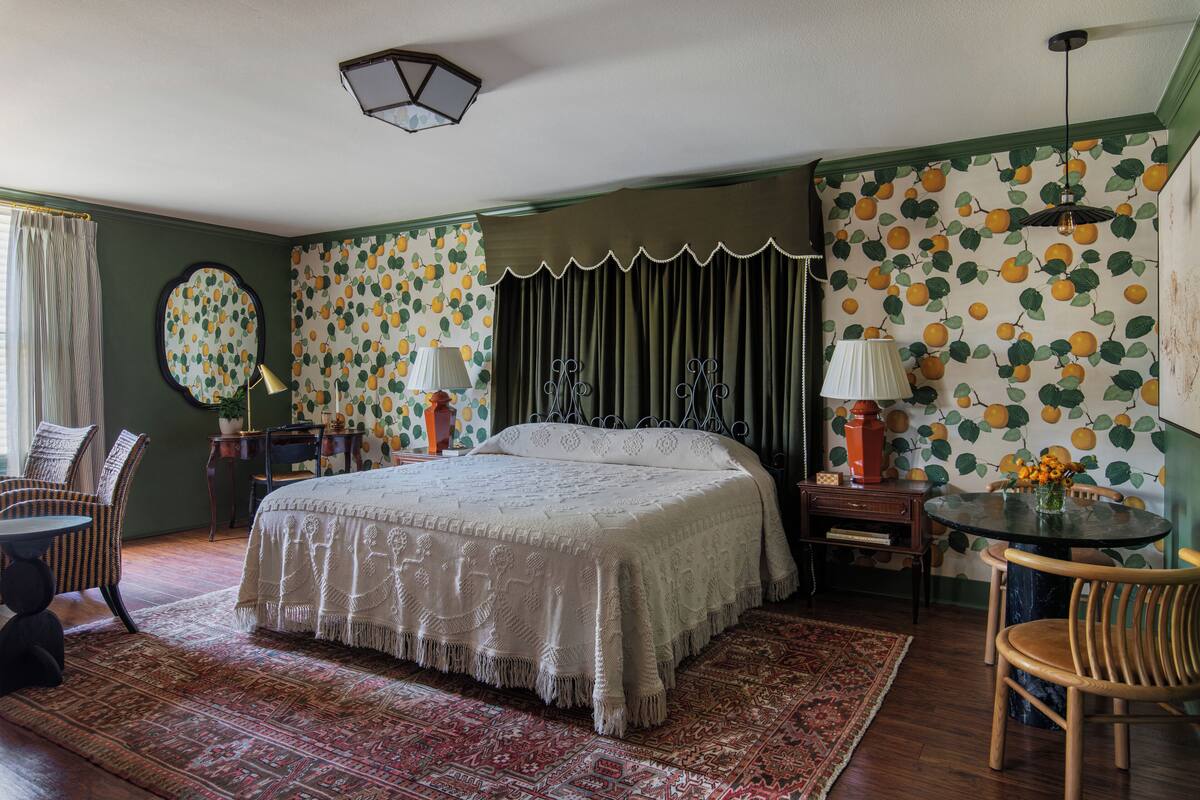 Une chambre avec un grand lit, une table ronde et une chaise. Il y a une lampe sur la table et une chaise à côté du lit.