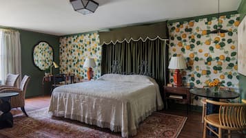 A bedroom with a large bed, a round table, and a chair. There is a lamp on the table and a chair next to the bed.