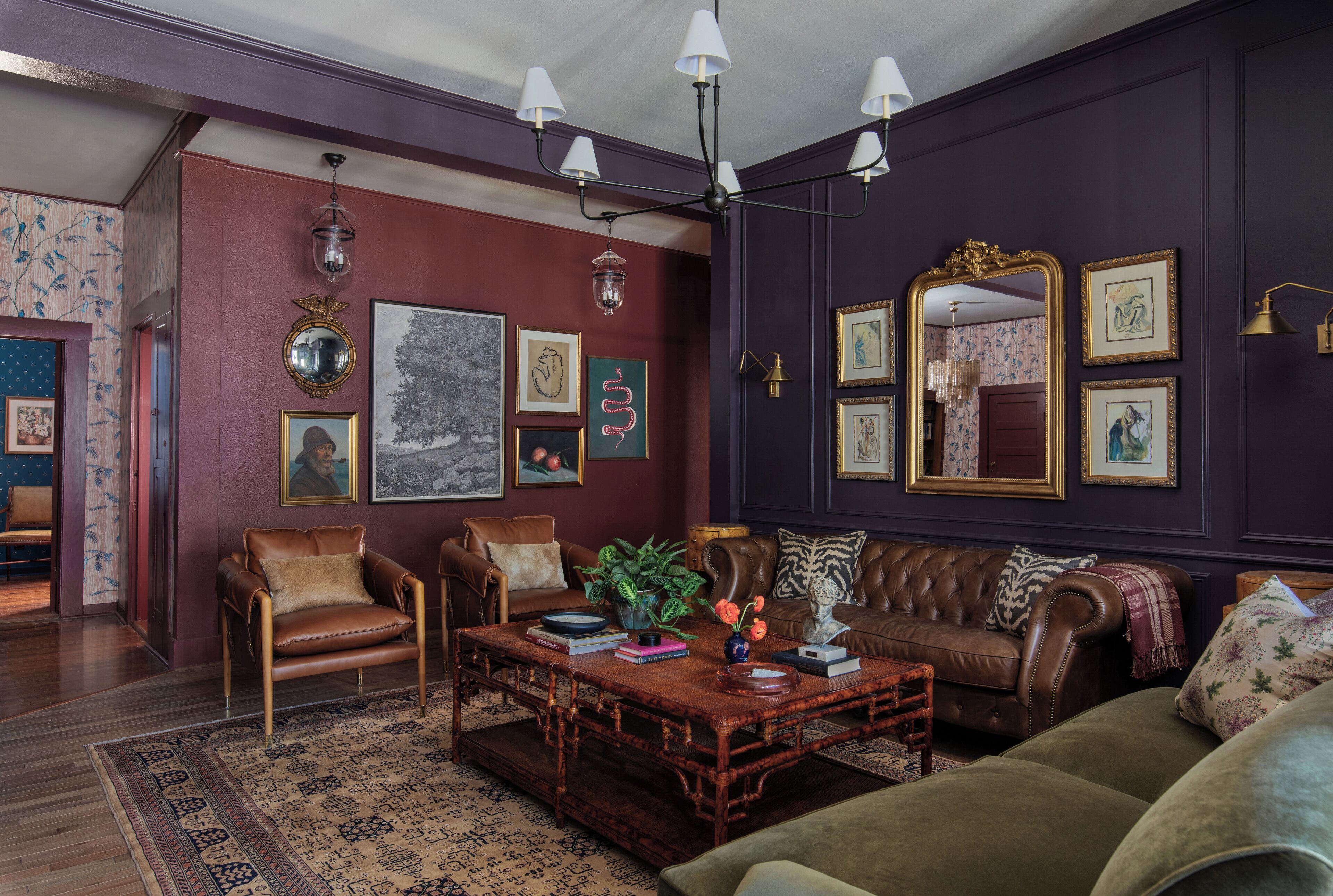 A room with a dark purple wall, a brown leather sofa, a wooden coffee table, and a patterned rug.